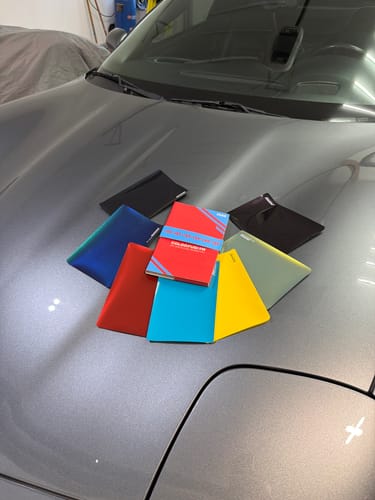 Reviewer showing the ColorFusion® PPF Sample Color Book with several large swatches fanned out on a gray car hood.