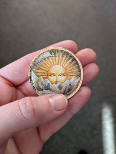 Customer holding the beautiful Memento Vivere Stoic Coin, showing its colorful sun and mountain design.