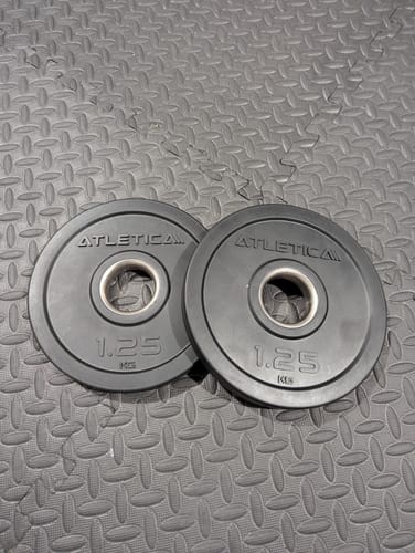 Ein Rezensent zeigt ein Paar schwarze 1,25 kg Rubber Plates, die auf einer strukturierten Fitnessmatte liegen.