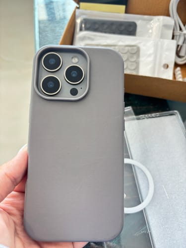 Customer holding the graphite grey Signature Leather Magsafe Case, showing the smooth back and camera fit.