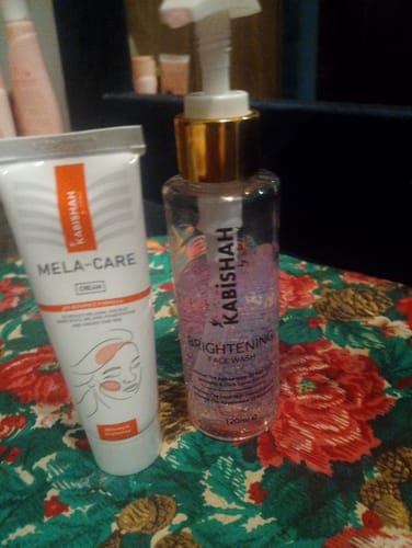 A reviewer's Pigmentation Bundle duo, the Mela Care Cream and Brightening Face Wash, on a floral surface.