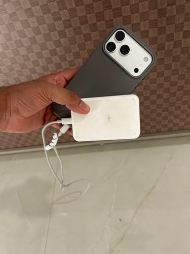 Customer's hand holding the graphite grey Signature Leather Magsafe Case with a MagSafe charger attached to the back.