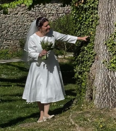 Cliente portant la robe trapèze blanche à manches trois-quarts comme robe de mariée en extérieur.