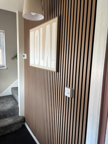 Reviewer's Premium Acoustic Slatted Wall Panel installed on a hallway wall, decorated with a large framed art piece.