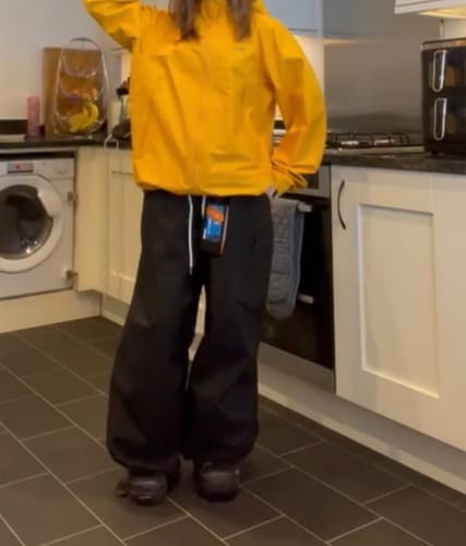 Customer wearing the baggy black snow pants with a yellow jacket in a kitchen, showing the overall fit.