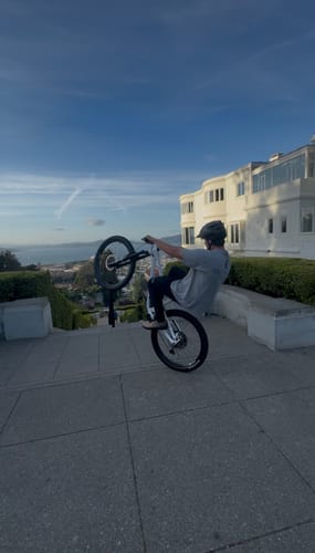 Customer performing a wheelie on a bicycle on a paved path overlooking a city.