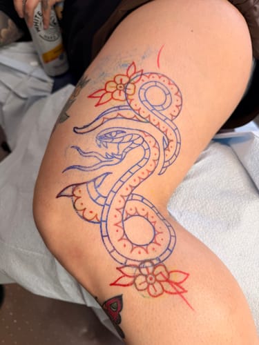 Customer's thigh with a snake and flower tattoo stencil in blue and red ink before the session.