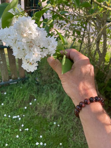 Un client portant le Bracelet Oeil de Taureau au poignet à côté de fleurs blanches dans un jardin.
