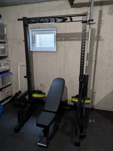 Kunde zeigt das aufgebaute R7 Half Rack mit Hantelbank und Langhantel in einem Heimstudio.