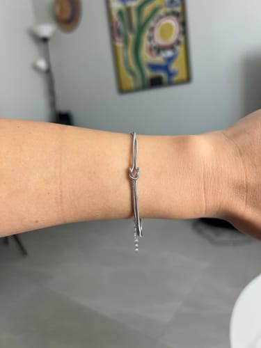 A close-up of a reviewer wearing a delicate silver bracelet with a knot design on their wrist.