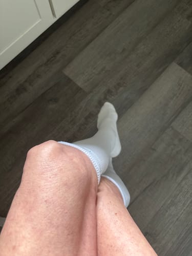 Reviewer sitting with their legs crossed wearing the white Performance Eucalyptus Compression Socks with the tops folded over.