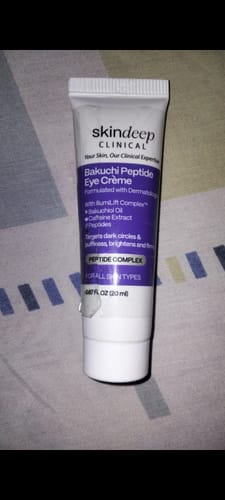 Customer's white and purple tube of Bakuchi Peptide Eye Crème standing on a patterned surface.