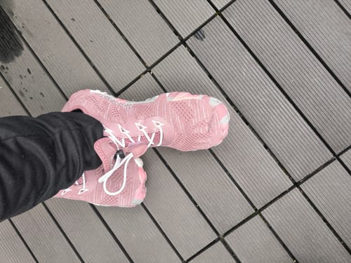 Ein Kunde trägt die rosa Smart II Barfußschuhe mit weißen Schnürsenkeln auf einem grauen Dielenboden.