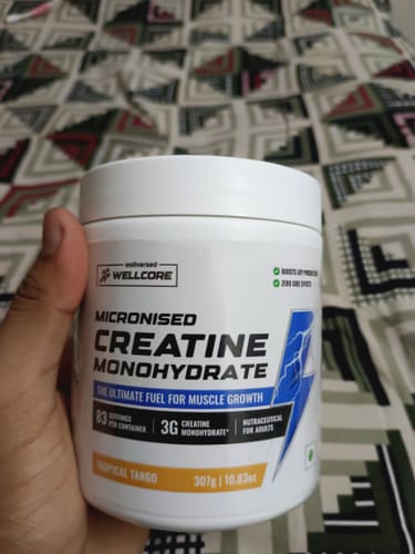 Customer's hand holds a tub of Wellcore Micronised Creatine Monohydrate in Tropical Tango.