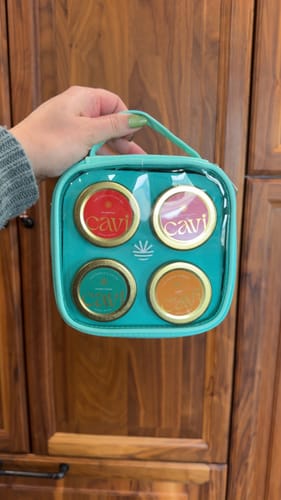 Reviewer holding a small teal case with a clear top, showing four jars of Cavi caviar inside.