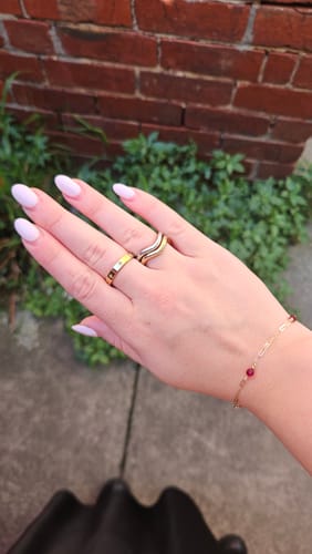 Customer's hand wearing the gold Star Studded Band stacked with another ring outdoors.