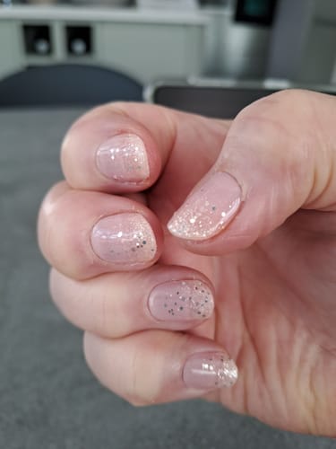 Customer's hand showing a fresh Pixie Dreams gel manicure with pale pink and silver glitter.