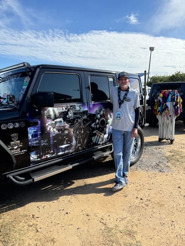 Reviewer wearing their Mississippi Blackout Plate Hat while standing outdoors next to a decorated vehicle.