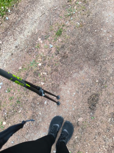 Kunde trägt die schwarzen Smart Ⅰ - Barfußschuhe auf einem Feldweg, mit Walkingstöcken in der Hand.