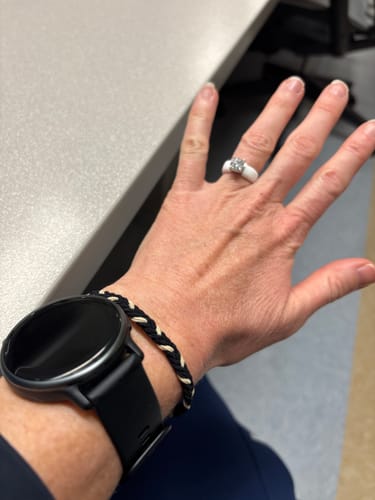 A reviewer's hand wearing the white Rinfit Silicone Ring with a solitaire stone at a desk.