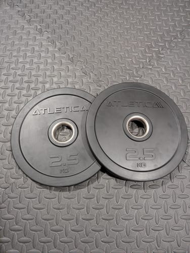 Kundenbewertung: Ein Paar schwarzer 2,5 kg Rubber Plates liegt auf einem strukturierten Fitnessboden.