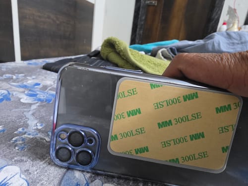 Customer's hand pressing the StickyPod, with its adhesive backing visible, onto the back of a smartphone case.