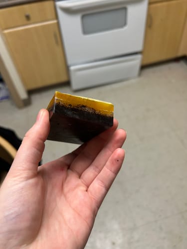 Customer holding a handmade two-tone soap bar with a dark bottom and a golden top layer.
