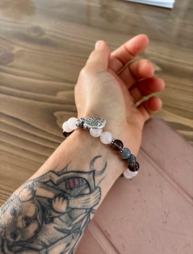 Client(e) portant le Bracelet Labradorite et Quartz Rose au poignet, posé sur une table en bois.