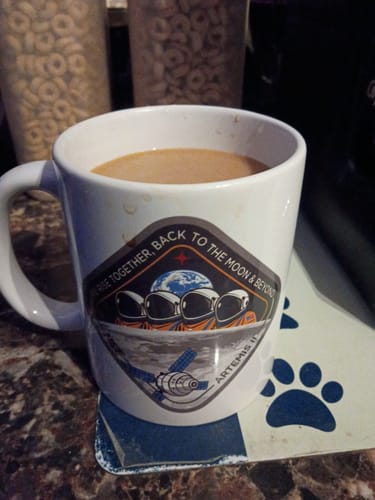 Customer's white Artemis II Mug filled with coffee, sitting on a counter with the mission design visible.