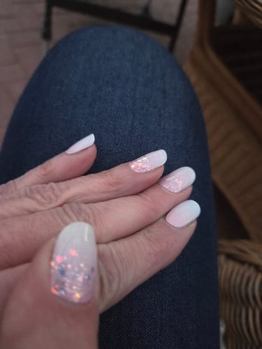 Hand einer Kundin, die die schönen Babyboomer Princess UV-Gelnägel mit blassem Design und Glitzerakzenten zeigt.