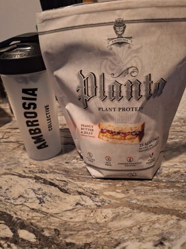 A reviewer's bag of Planta Premium Plant Protein in Peanut Butter & Jelly flavor, sitting next to a shaker bottle on a counter.
