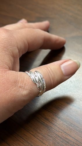 Customer wearing the silver Feather From An Angel Ring on their thumb, resting on a wooden surface.