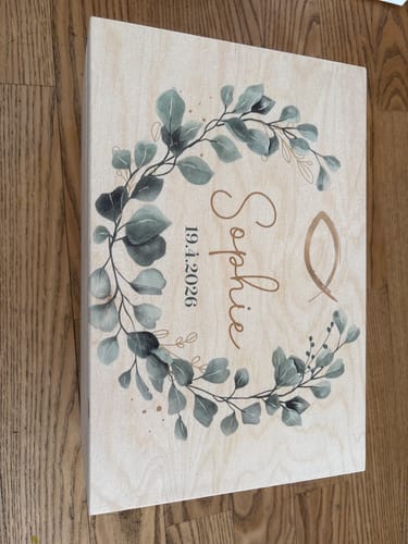 Kunde zeigt die geschlossene personalisierte Erinnerungskiste mit Eukalyptus-Design auf einem Holzboden.