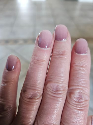 Nahaufnahme der Hand einer Kundin mit kurzen, glänzenden Evening Out Ombré UV-Gelnägeln.