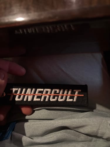 Reviewer holds their HEARTBREAKER JET TAG, showing the black embroidered 'Tuner Cult' side.