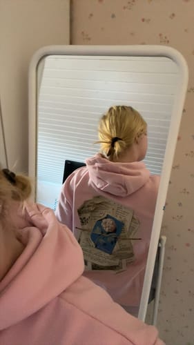 Reviewer showing the back graphic of the oversized newspaper pink hoodie in a mirror.