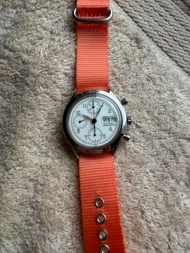 Reviewer's Alpha3 - Tango Tangerine strap on a silver chronograph watch, showing the bright orange nylon and metal grommets.
