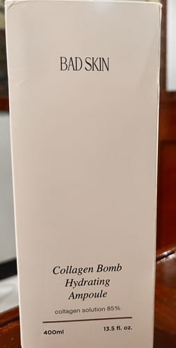 Reviewer shows the white box of the Bad Skin Collagen Bomb Hydrating Ampoule.