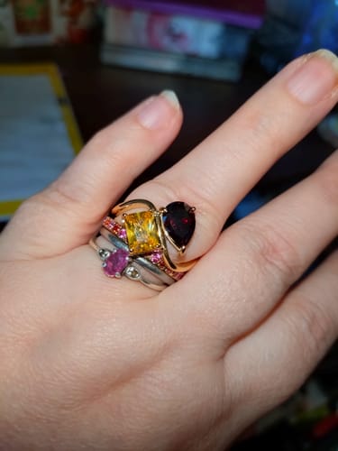 Customer's hand wearing the gold Navae Birthstone Ring with a yellow and a deep red stone, stacked with other rings.
