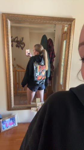 Reviewer's mirror selfie showing the colorful back graphic and baggy fit of the black Demon Slayer hoodie.