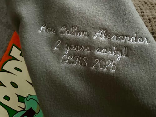 Close-up of custom white embroidery on the grey fleece back of a customer's Project Repat T-Shirt Quilt.