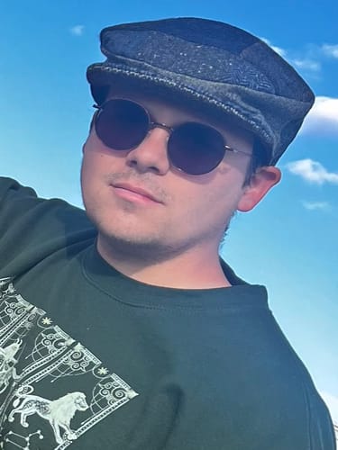Customer wearing the grey and blue patchwork Vintage Cap outdoors against a blue sky.
