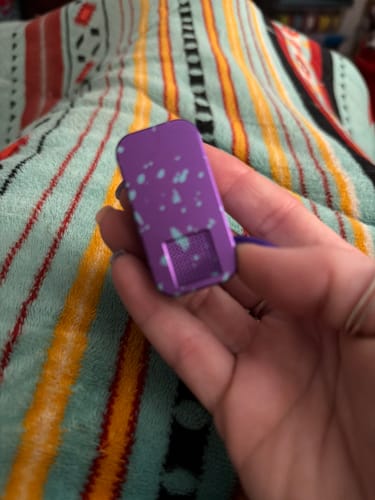 Reviewer's hand holding a speckled purple pill case against a colorful striped background.