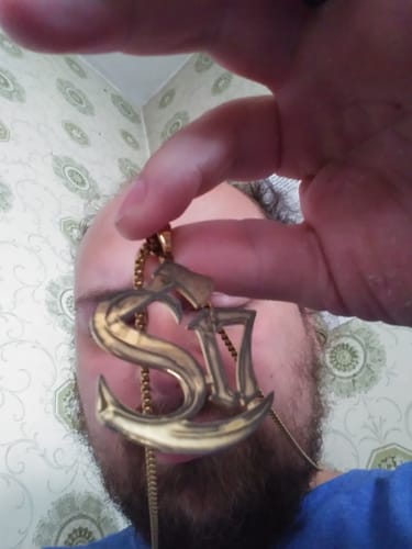 Close-up of a reviewer holding a custom gold-colored logo pendant shaped like an S-anchor on a ball chain.