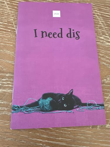 Customer's purple February 2026 Booklet with a cover image of a black cat playing with yarn.
