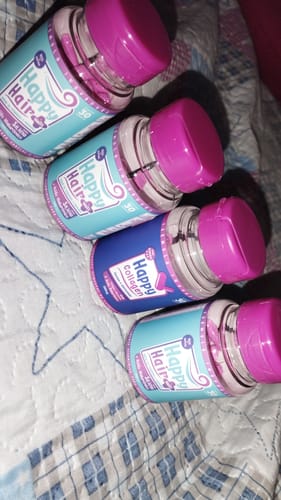 Cliente exibe os três potes de Happy Hair e o pote de Happy Collagen deitados sobre uma superfície de tecido.