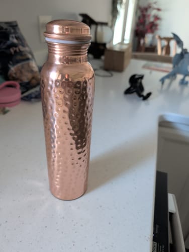 Customer's hand-hammered Pure Copper Water Bottle standing on a white kitchen counter.