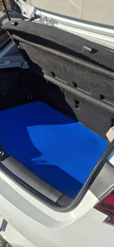 Klient pokazuje niebieską matę do bagażnika na wymiar umieszczoną w bagażniku białego samochodu.