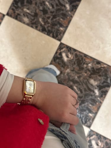 Reviewer's wrist with the gold CLAIRE DE MAINS watch, shown against a red sleeve and tiled floor.