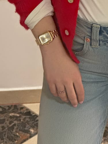 Close-up of a reviewer wearing the elegant, gold CLAIRE DE MAINS watch with a red cardigan.